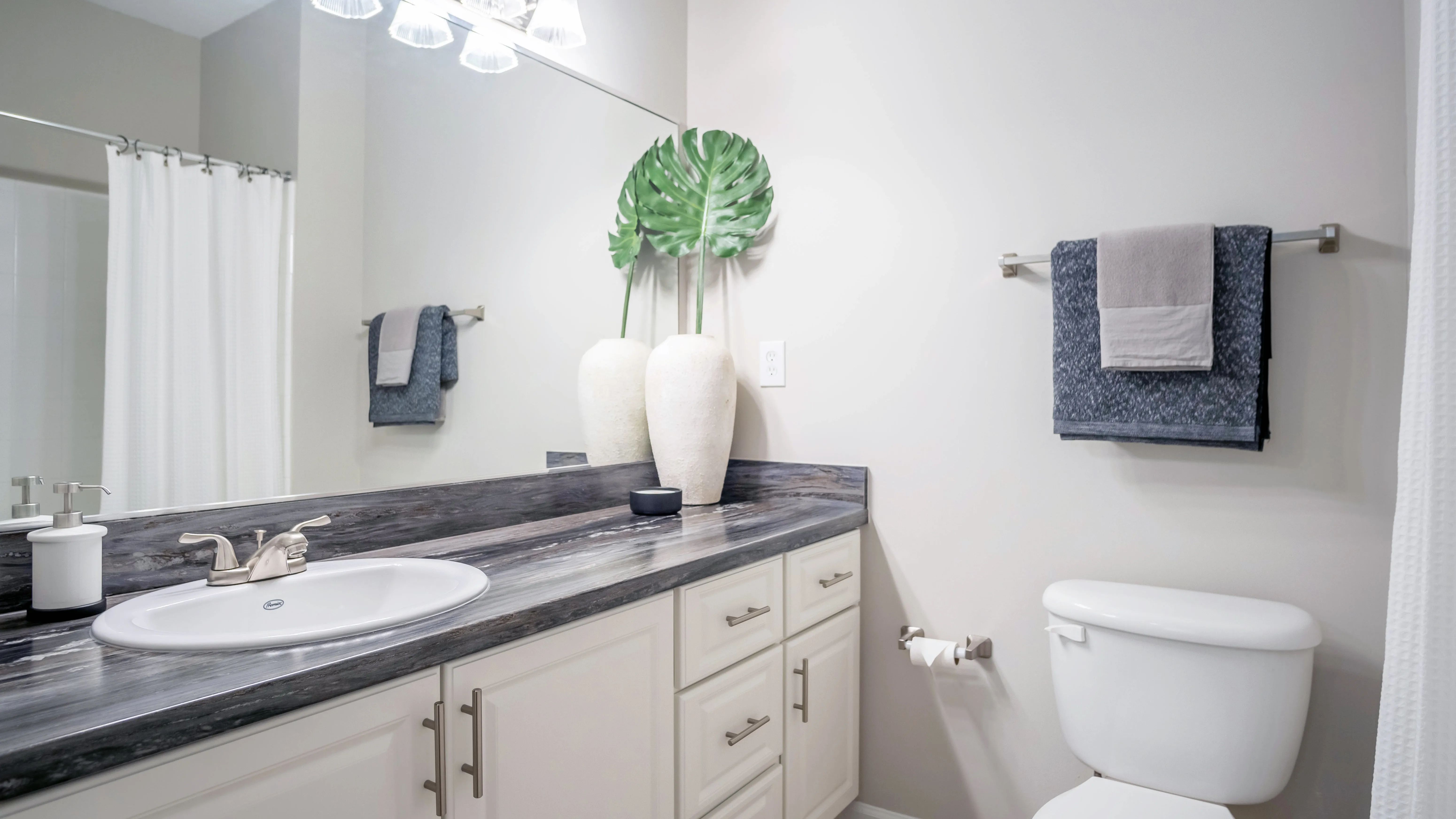 Our exquisite bathrooms feature black fusion countertops, expansive mirrors with vanity lighting, and luxurious tile flooring.