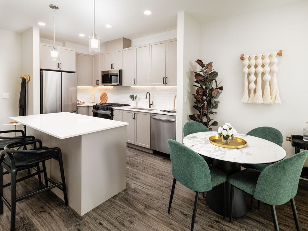 Kitchen and dining area with grey cabinetry, white quartz countertops, white tile backsplash, stainless steel appliances, and pendant lighting