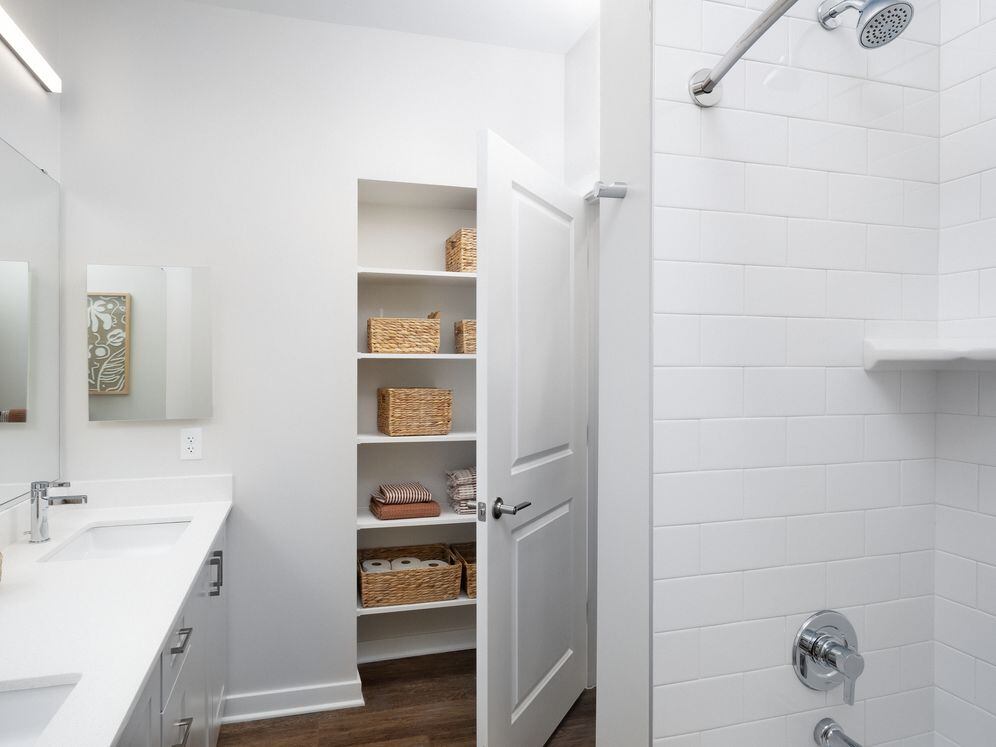 New West Phase apartments - Finish Package III Bathroom with white quartz countertops, grey cabinetry, hard surface flooring, and built in storage closet