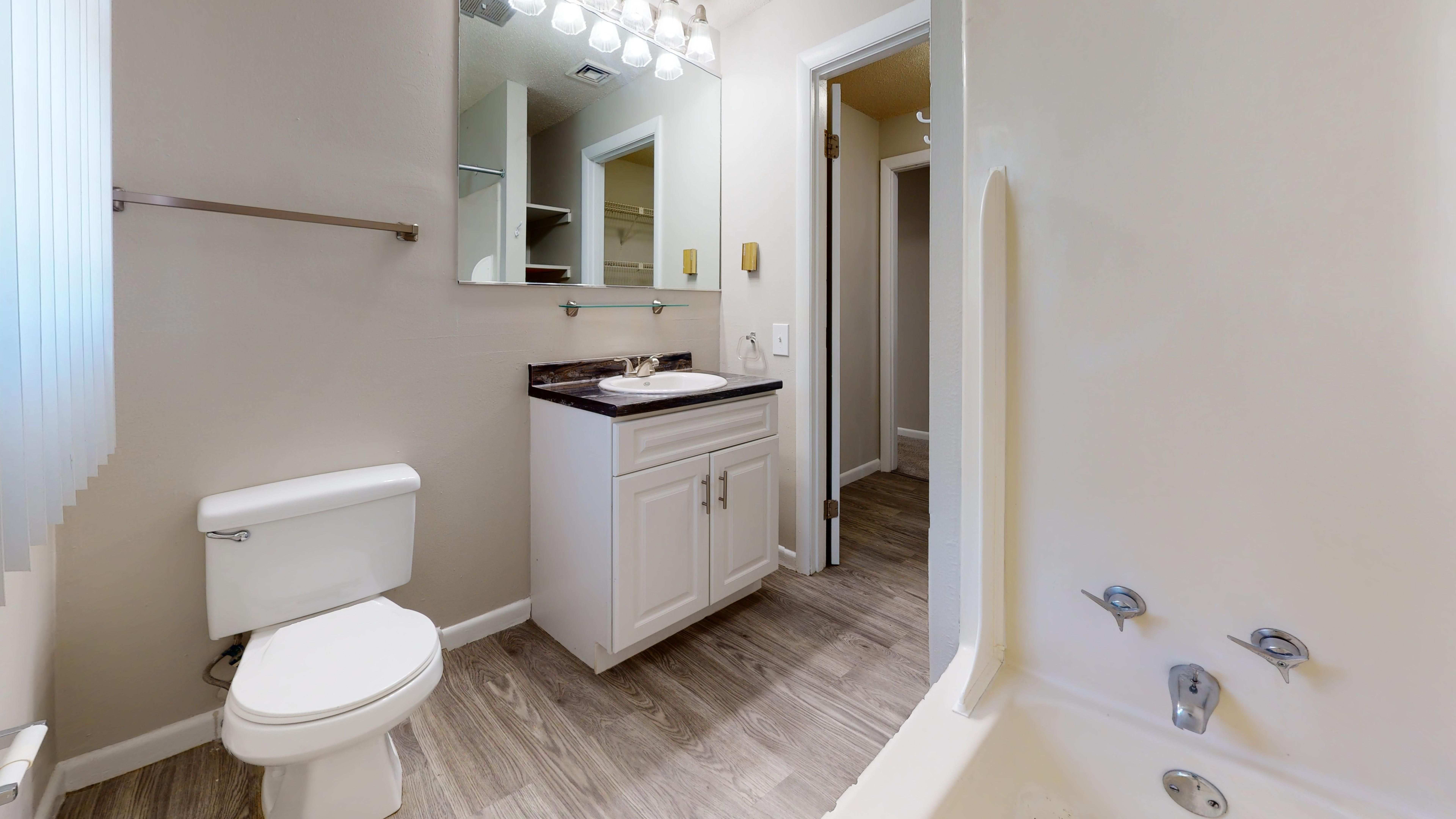 The bathroom in The Pioneer layout features a deep soaking tub, contemporary vanity, and wood-style flooring.