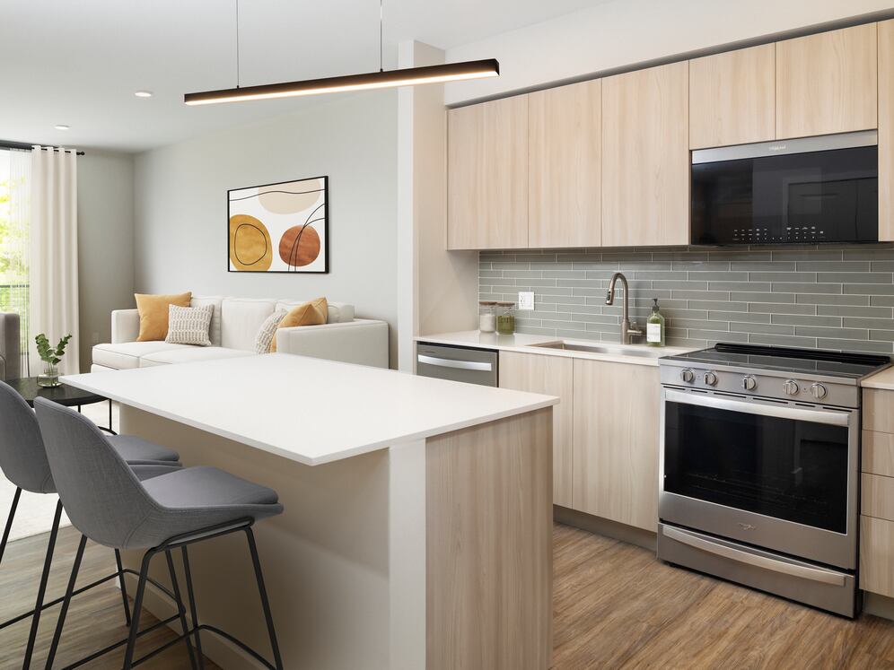 Upgrade Collection I One-bedroom apartment kitchen with light wood cabinetry, grey tile backsplash, white quartz countertops, and stainless steel appliances