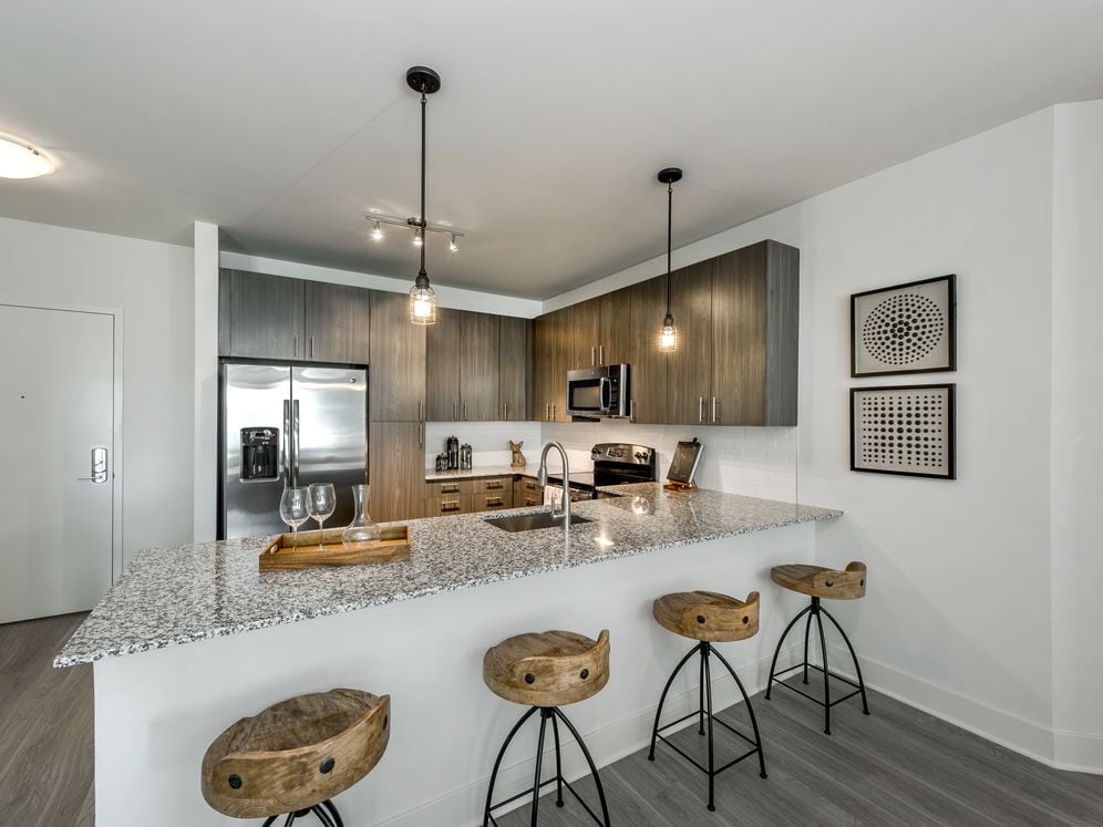 Open concept kitchen with brown cabinetry, granite countertops, stainless steel appliances, tile backsplash and hard surface flooring