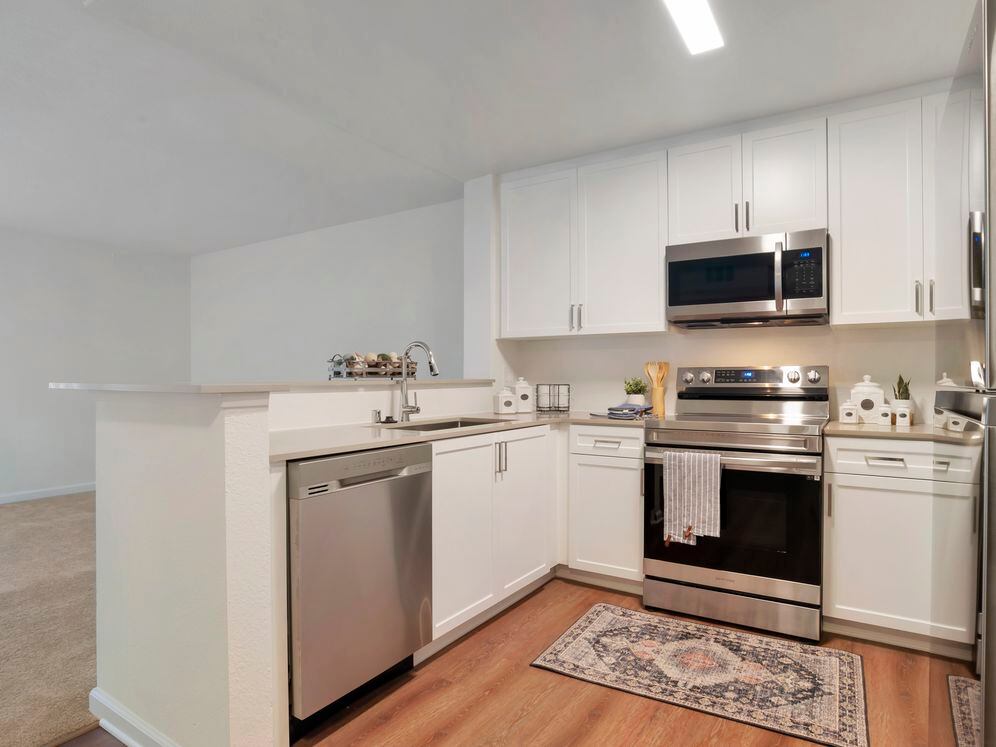 Kitchens with stainless steel appliances, beige quartz countertops, white cabinetry, and hard surface flooring