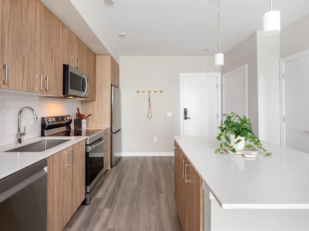 Finish Package II Kitchen with oak cabinetry, white quartz countertops, stainless steel appliances, pendant lighting, and hard-surface vinyl plank flooring