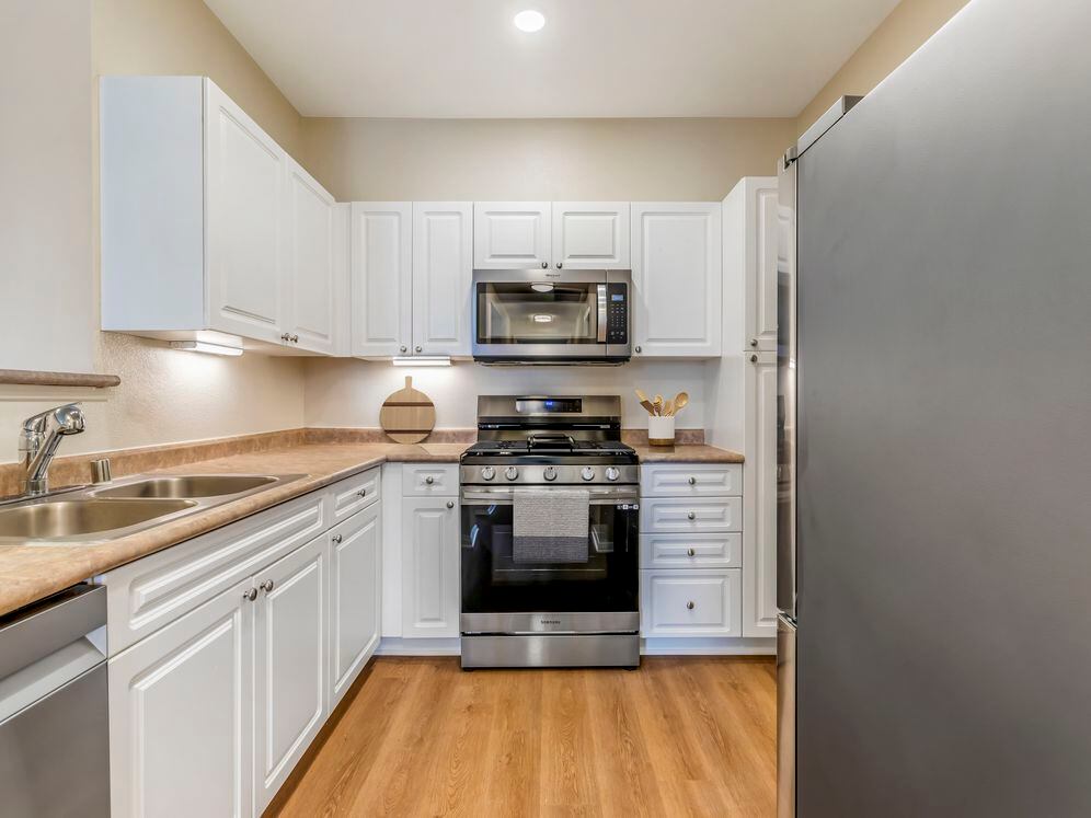 Classic Package II kitchen with upgraded stainless steel appliances, white cabinetry, neutral laminate countertops, and upgraded hard surface flooring