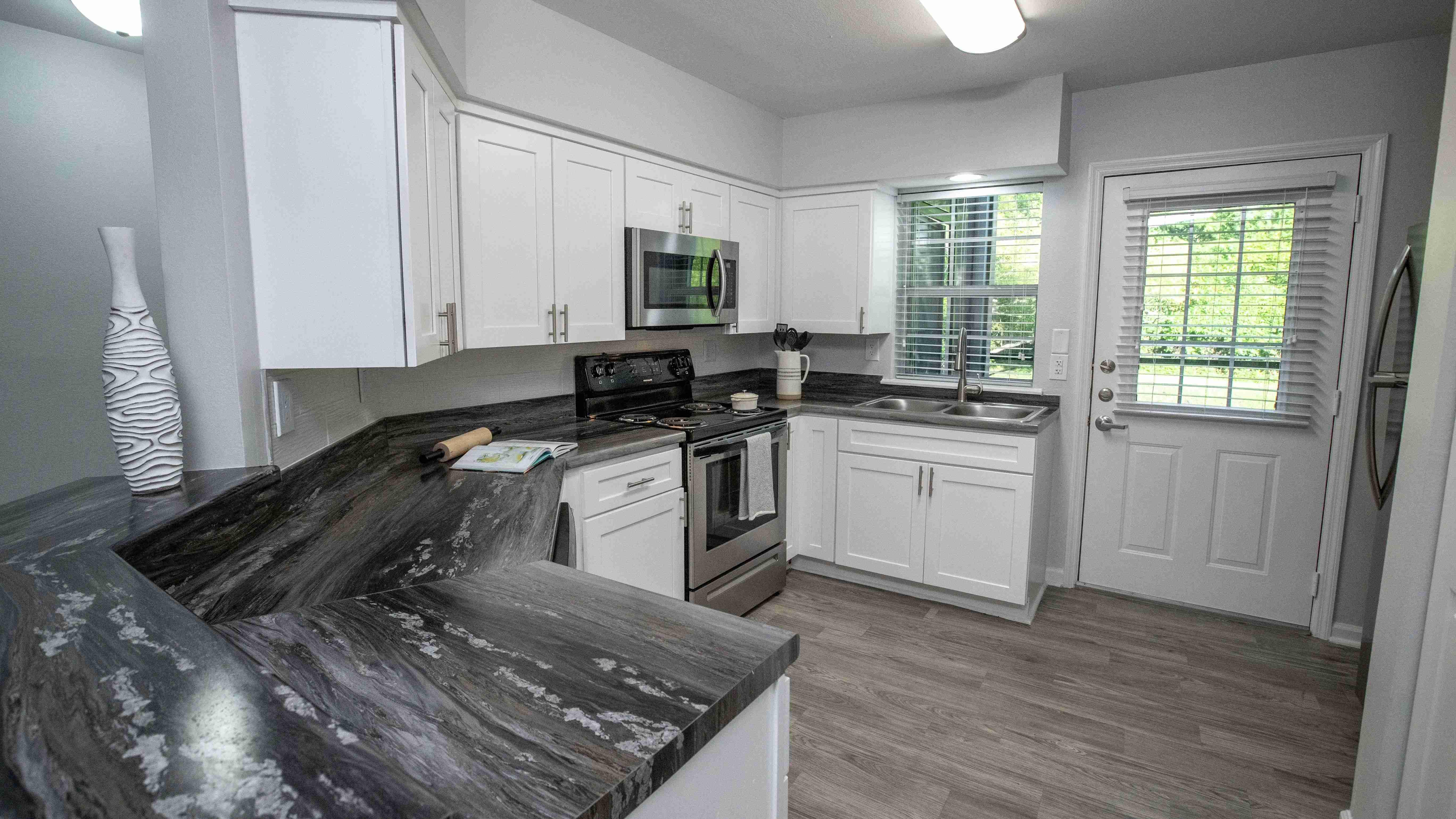 Sleek black fusion countertops, abundant white shaker cabinetry, and stainless-steel appliances create an elegant and functional culinary haven in this spacious kitchen with a breakfast bar.