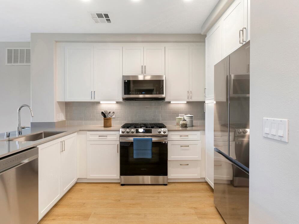 Renovated Package I kitchen with stainless steel appliances, grey quartz countertops, white cabinetry, grey tile backsplash, and hard surface flooring