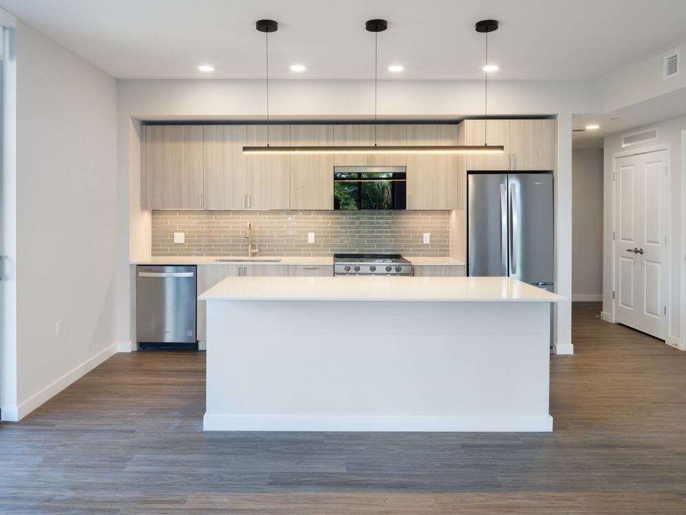Upgrade Collection I kitchen with light wood cabinetry, grey tile backsplash, white quartz countertop, and stainless steel appliances