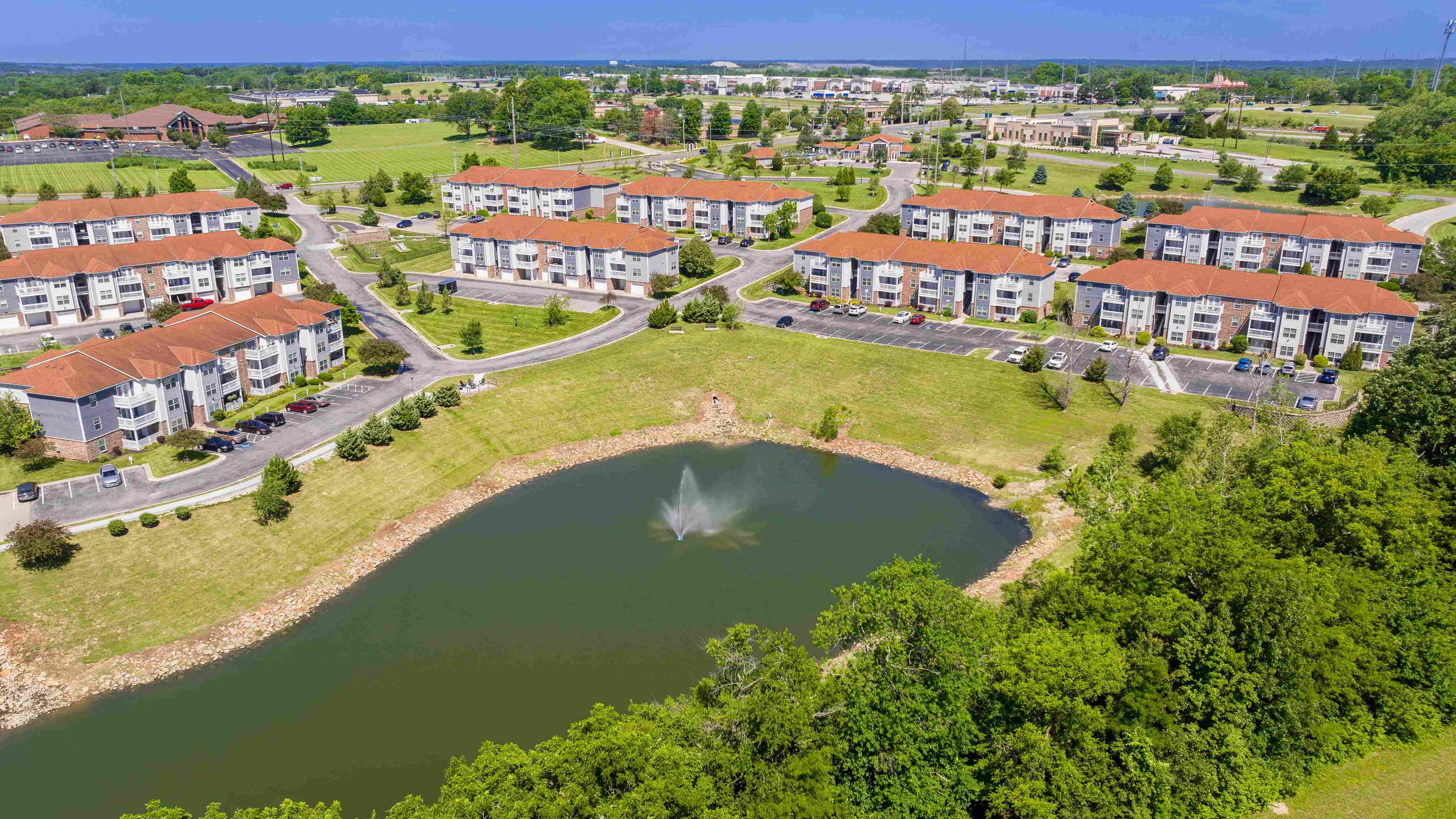 Explore the expansive grounds of Lenox West from above, featuring charming buildings, well-maintained landscapes, and a picturesque pond with a fountain.