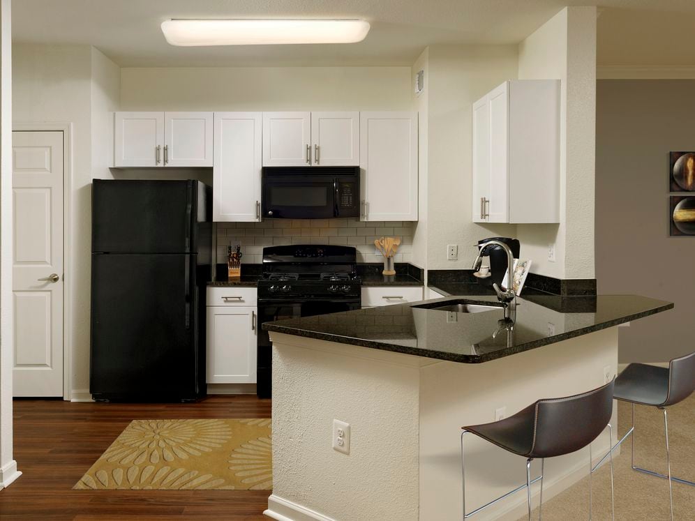 Renovated Package II kitchen with white cabinetry, black granite countertops, black appliances, white tile backsplash, and hard surface plank flooring