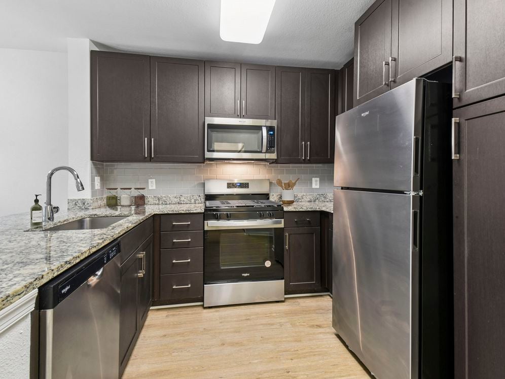 Renovated Package I kitchen with espresso cabinetry, speckled granite countertops, beige subway tile backsplash, stainless steel appliances, and hard surface flooring
