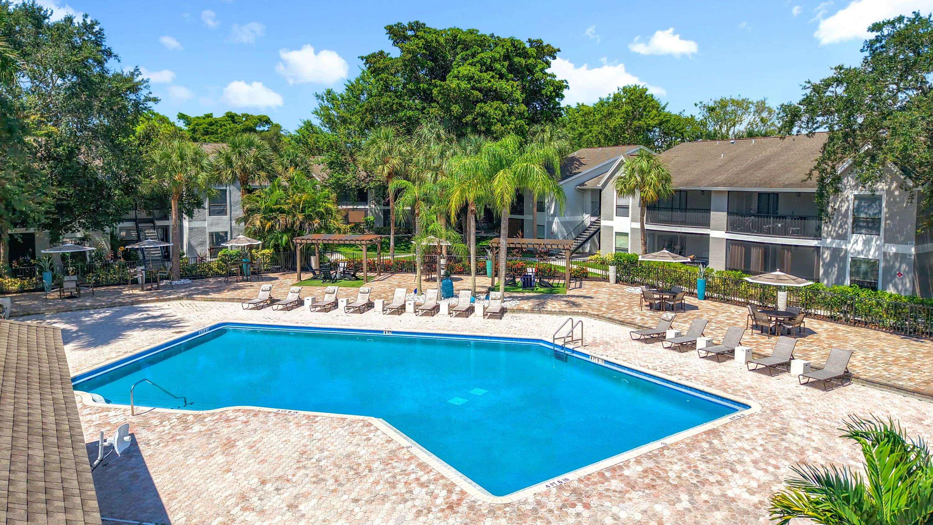 Dive into relaxation at our sparkling swimming pool surrounded by lush landscaping, lounge chairs, umbrellas, and shaded pergola seating for a true resort-style retreat.