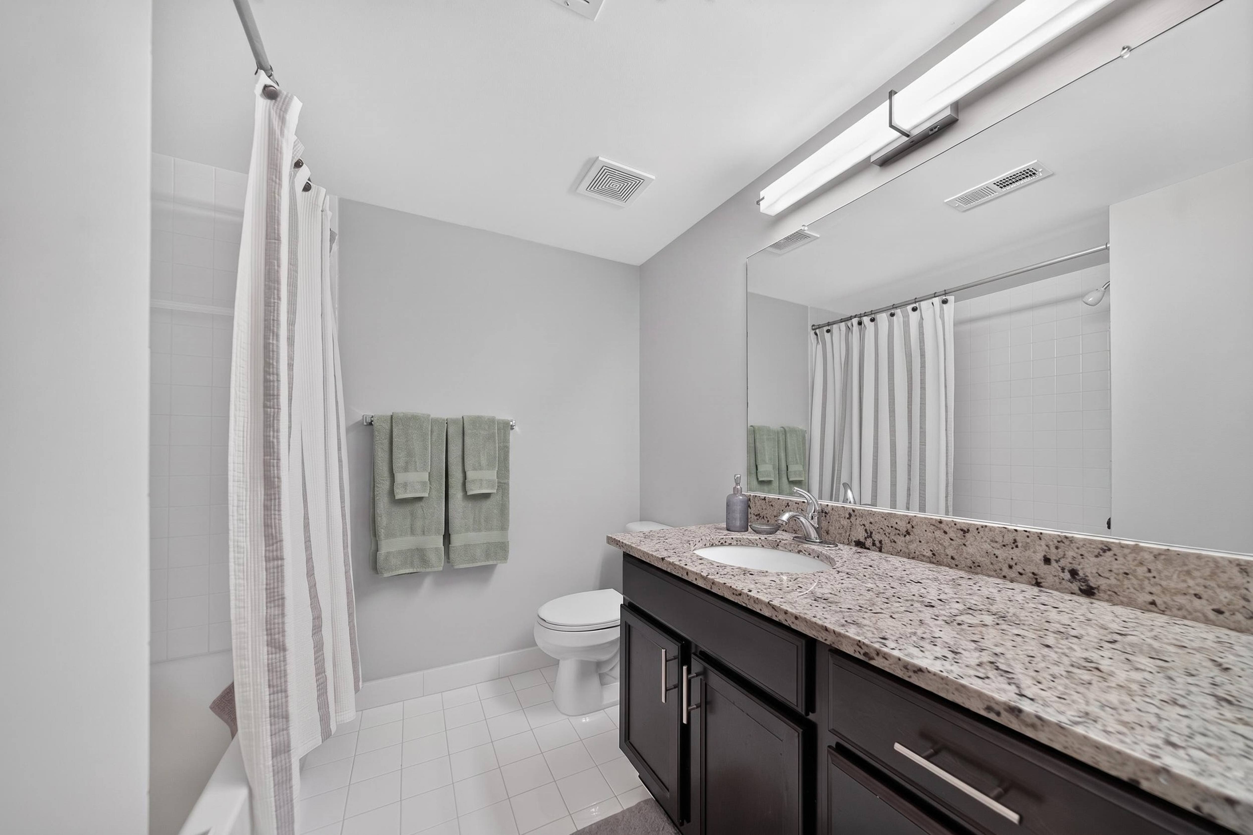Modern bathroom with large vanity mirror and tub/shower at Lakeside Village Apartments in Clinton Township, MI