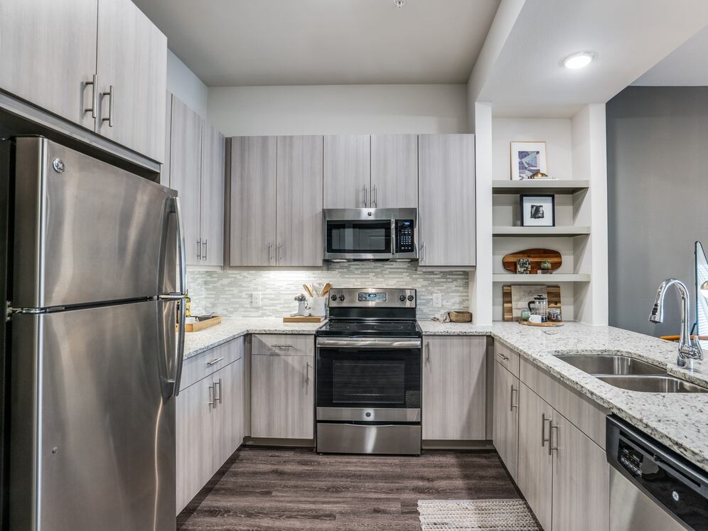 Gray finish package kitchen with speckled granite countertop, stainless steel appliances, and hard surface flooring.