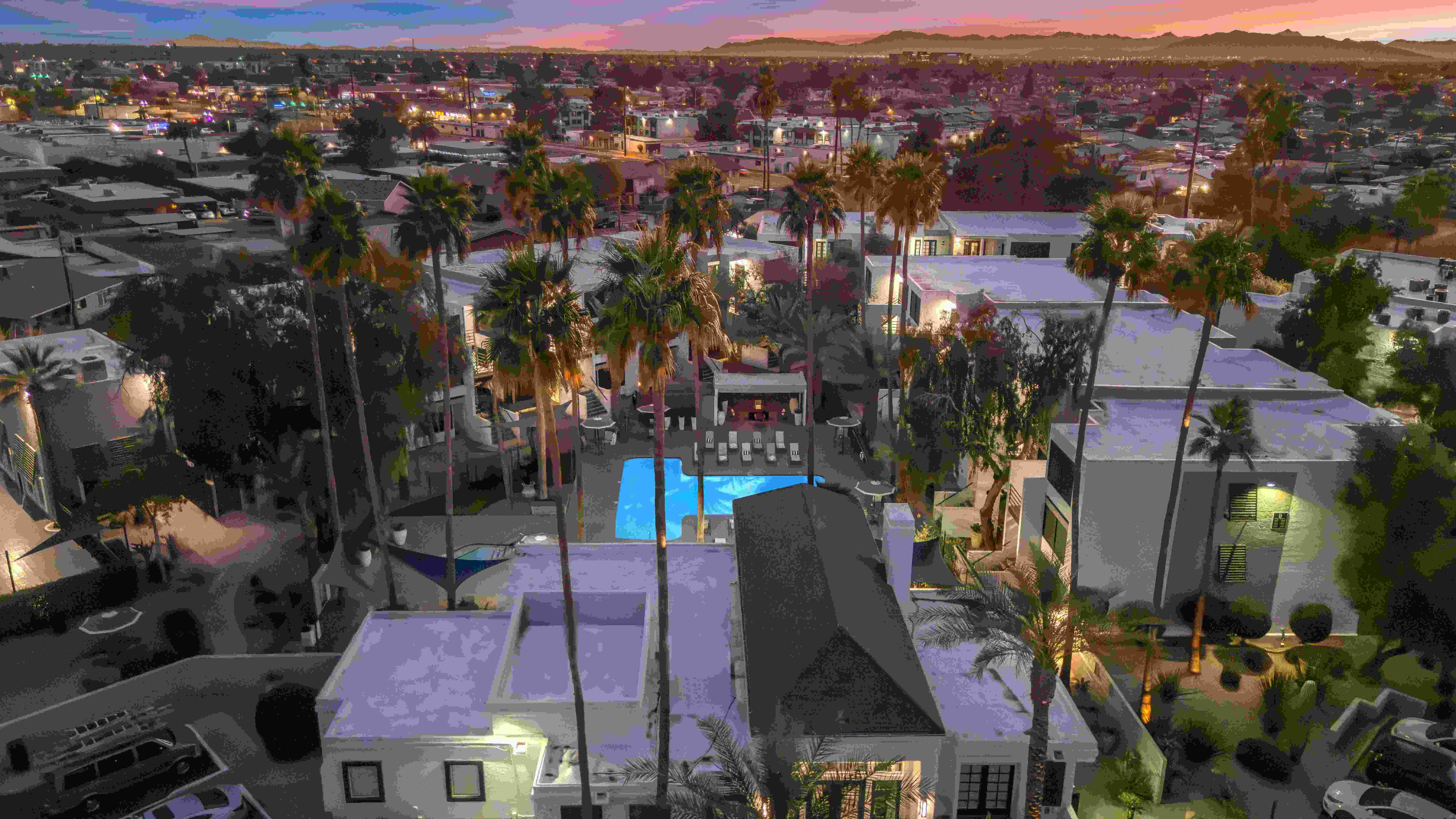 An enchanting aerial view of Beacon at 601 as the sun sets, casting a vibrant glow over the sky. The shimmering resort-style pool, elegant cabana seating, and palm-lined pathways create a serene escape, perfect for unwinding after a long day.
