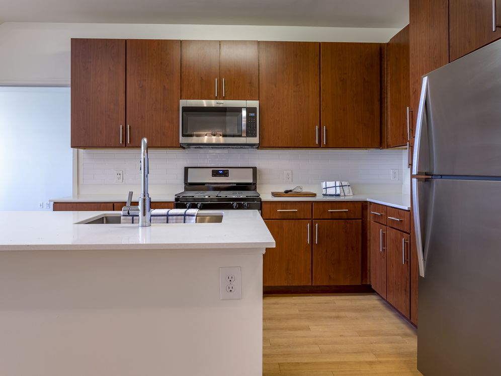 Newly renovated apartment homes feature kitchens with cherry cabinetry, white quartz countertops, stainless steel appliances, white tile backsplash, and hard surface flooring