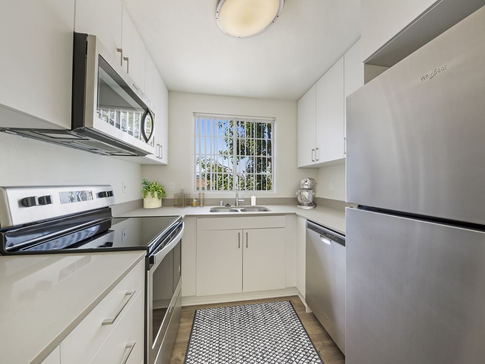 Upgraded Package kitchen with white cabinetry, grey quartz countertops, stainless steel appliances, upgraded lighting and fixtures, and hard surface flooring throughout