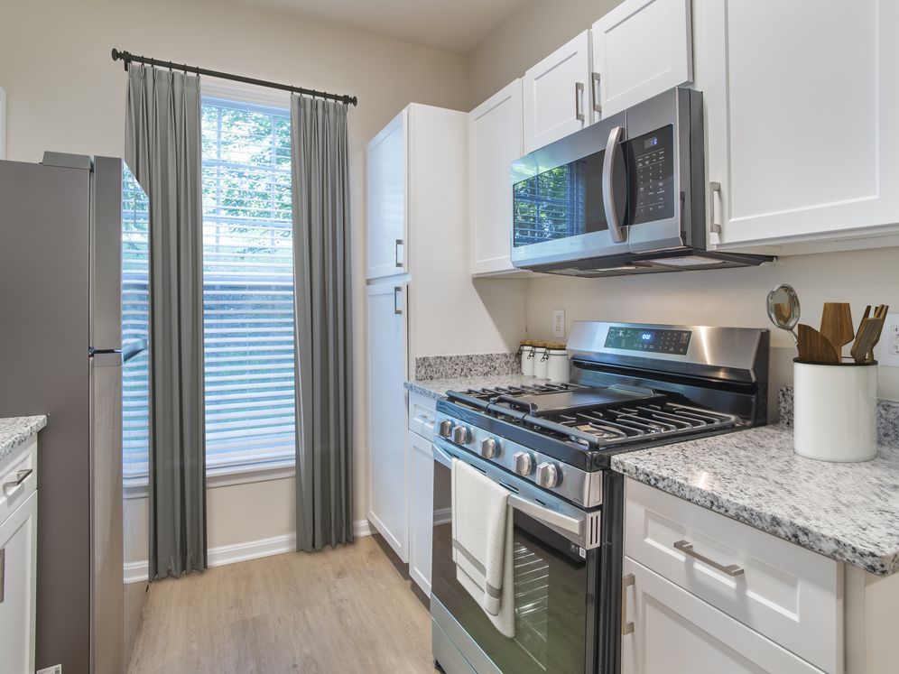 Renovated Package II kitchen with stainless steel appliances, white speckled quartz countertops, white cabinetry, and hard surface flooring