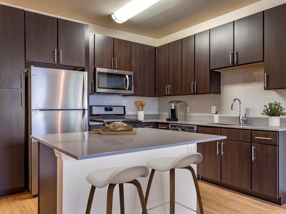 Newly renovated apartment homes feature kitchens with espresso cabinetry, grey quartz countertops, stainless steel appliances, grey tile backsplash, and hard surface flooring