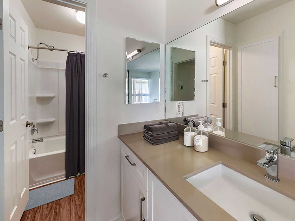 Renovated Package I bath with beige quartz countertops, new white cabinetry, and hard surface flooring