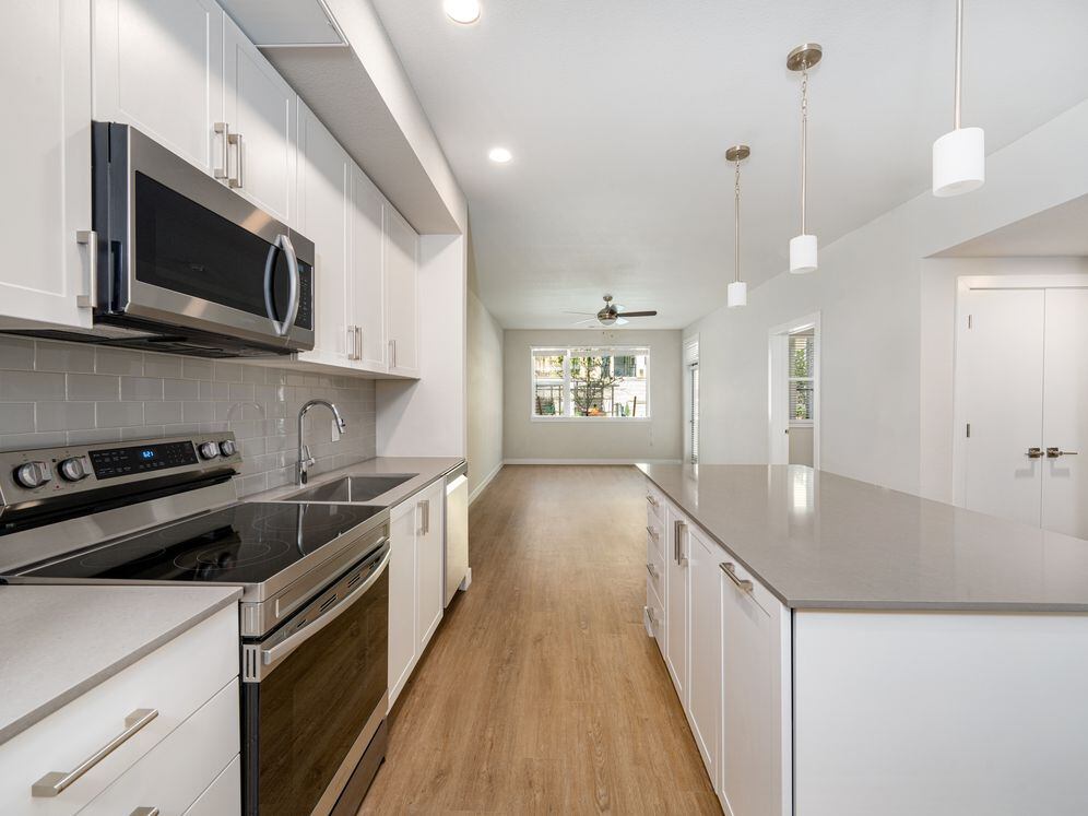 Finish Package I Kitchen with white cabinetry, grey quartz countertops, grey tile backsplash, stainless steel appliances, and hard-surface vinyl plank flooring