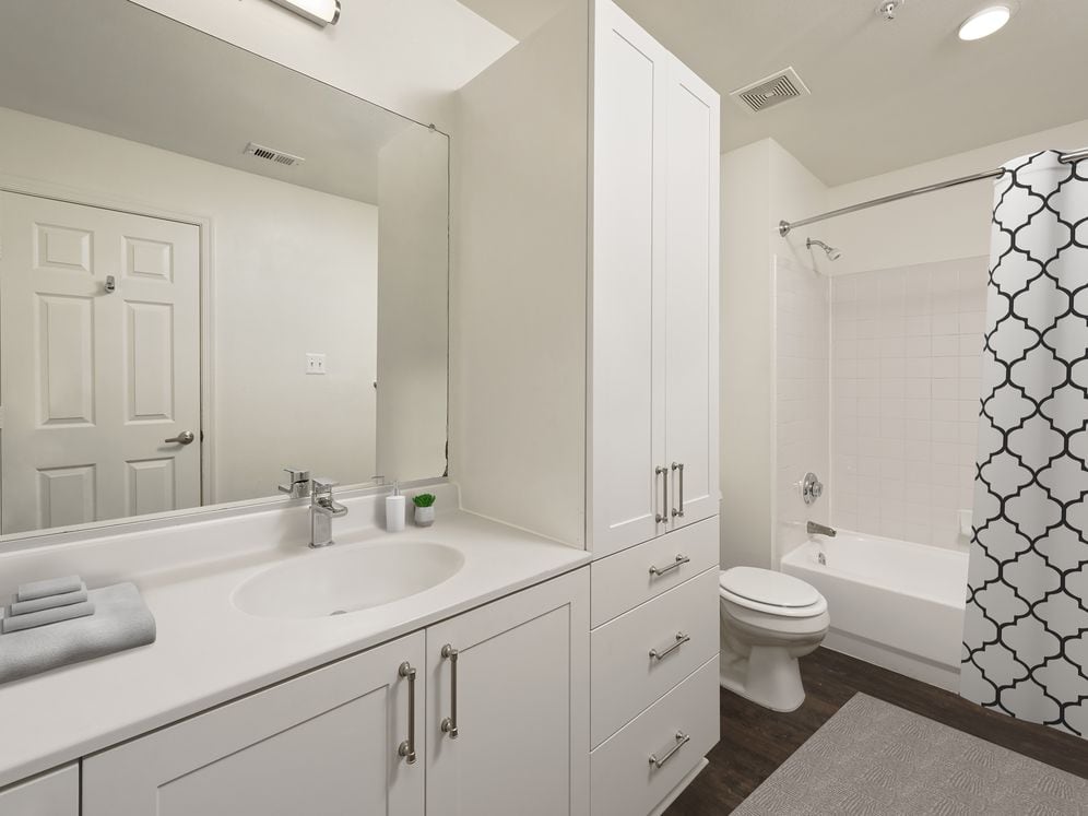 Renovated Package II bath with white cultured marble countertops, white cabinetry, and hard surface flooring