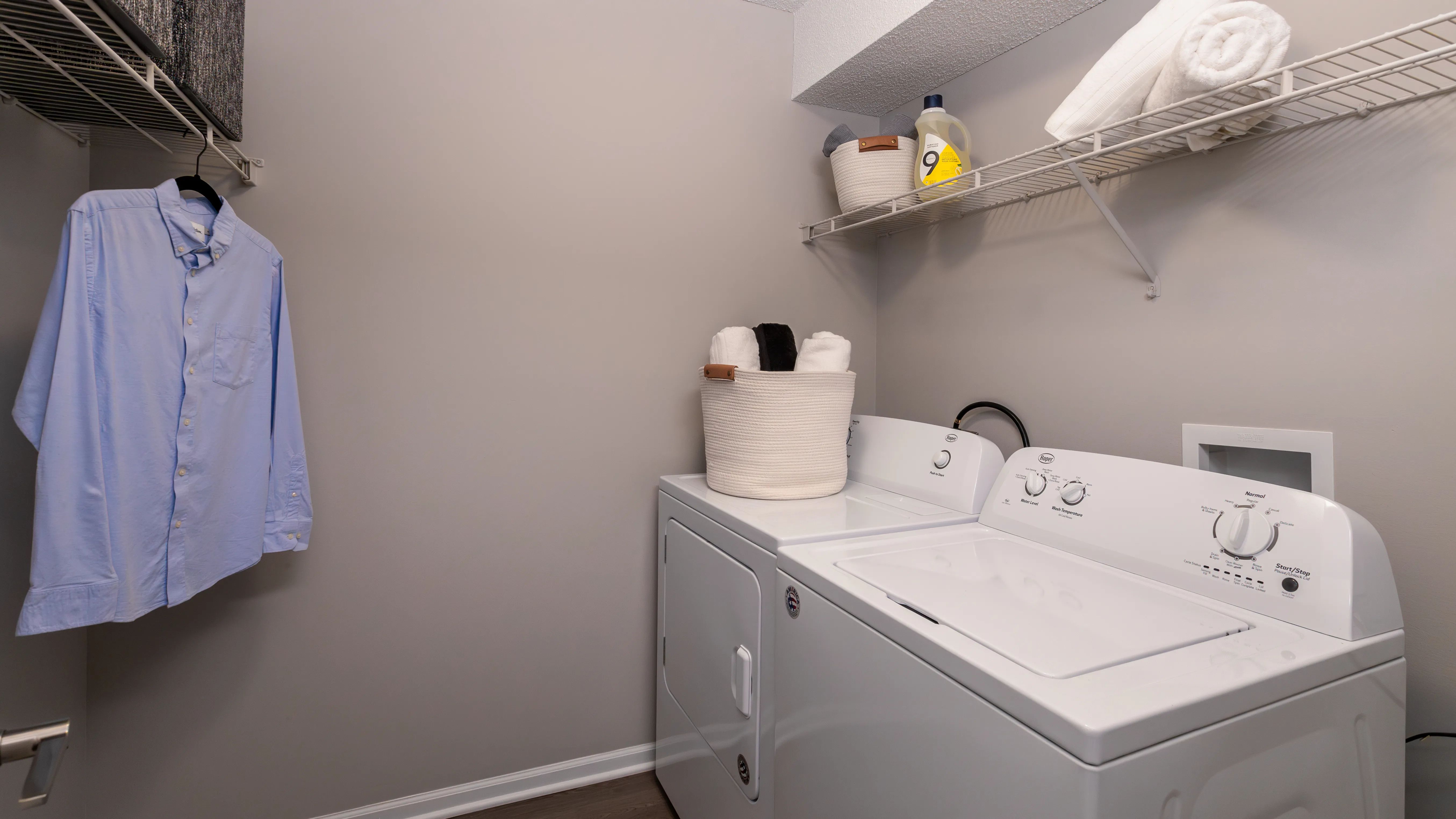 Convenient in-unit laundry facilities featuring a full-size washer and dryer, ample shelving, and hanging space.