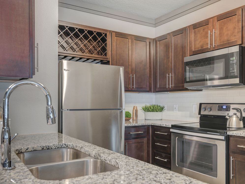 Modern kitchen with wood cabinetry, white tile backsplash, granite countertops, and stainless steel appliances