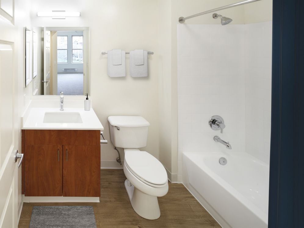 Renovated Package I bath with white quartz countertops, oak cabinetry, and hard surface flooring
