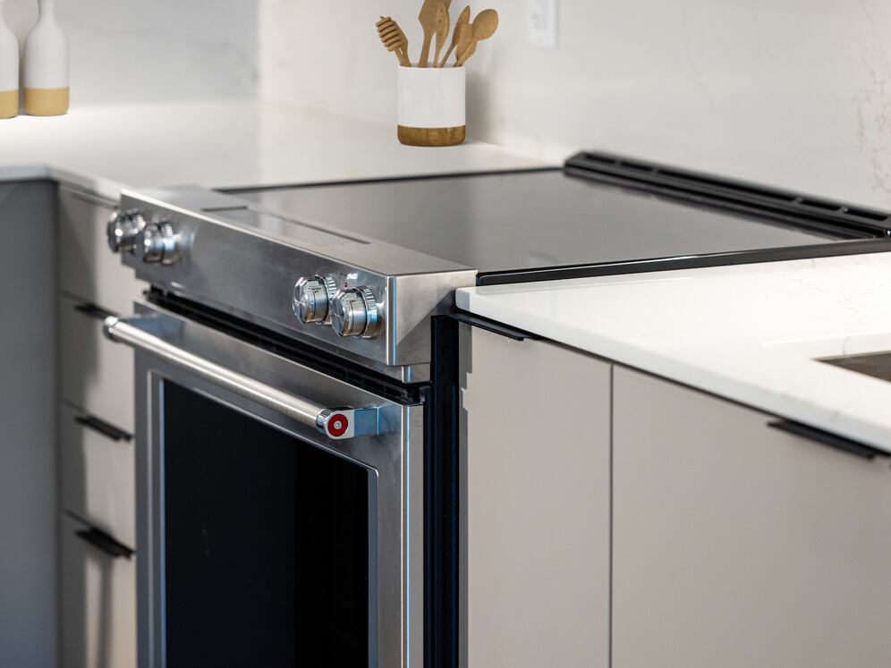 Signature Collection kitchen with light grey cabinetry, electric stove, and marbled quartz countertops and backsplash