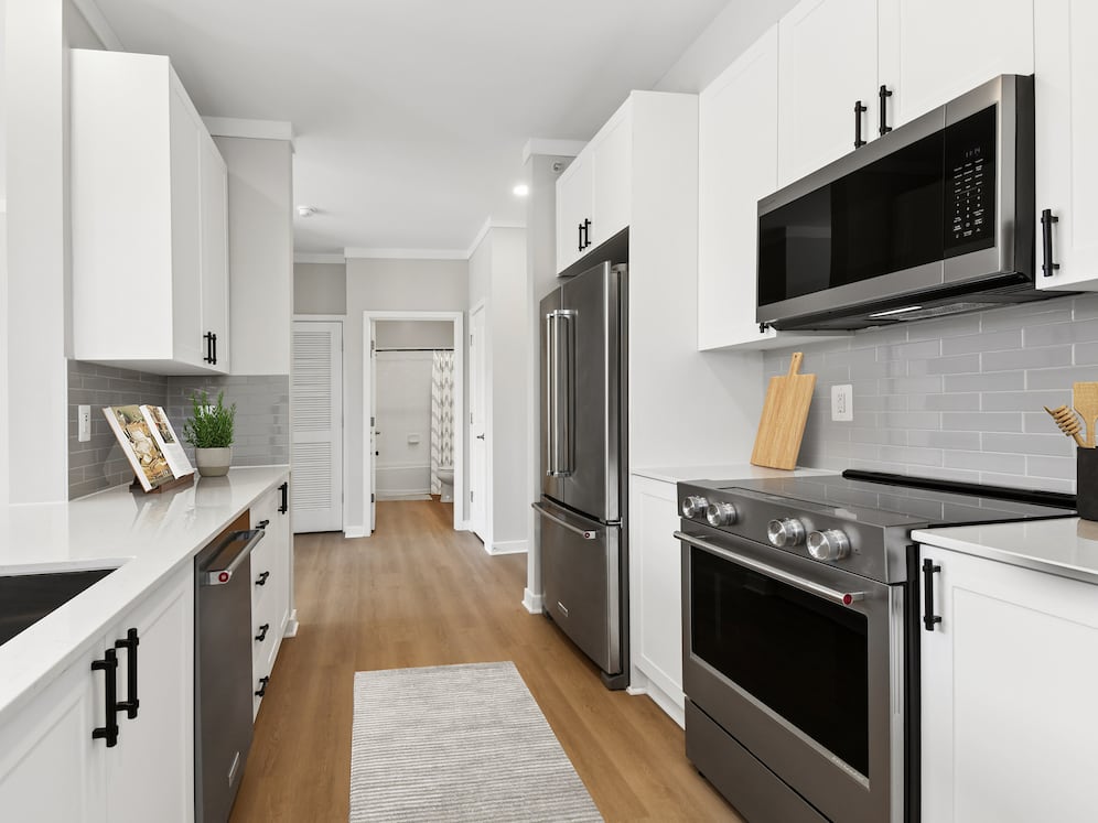 Renovated Package II kitchen with stainless steel appliances, white cabinetry, grey tile backsplash, white quartz countertops, and hard surface flooring