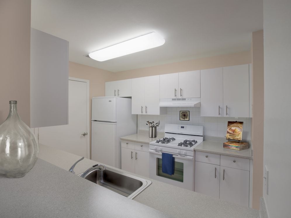Classic Package kitchen with white cabinetry, laminate countertops, extended hard surface flooring (in select units), white appliances, and white tile backsplash