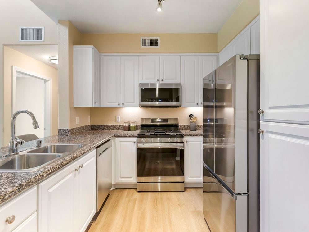 Renovated Package I kitchen with stainless steel appliances, beige speckled granite countertop, white cabinetry, and hard surface flooring