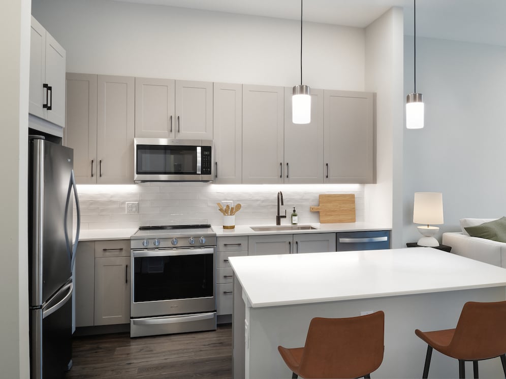 Upgrade Collection II kitchen with stainless steel appliances, grey cabinetry, white quartz countertops, tile backsplash, under-cabinet lighting, and hard-surface flooring