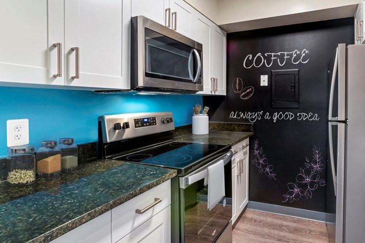 Renovated Package II kitchen with new white cabinetry, granite countertops, stainless steel appliances, painted backsplash, chalkboard accent wall, upgraded lighting and fixtures, and hard surface flooring