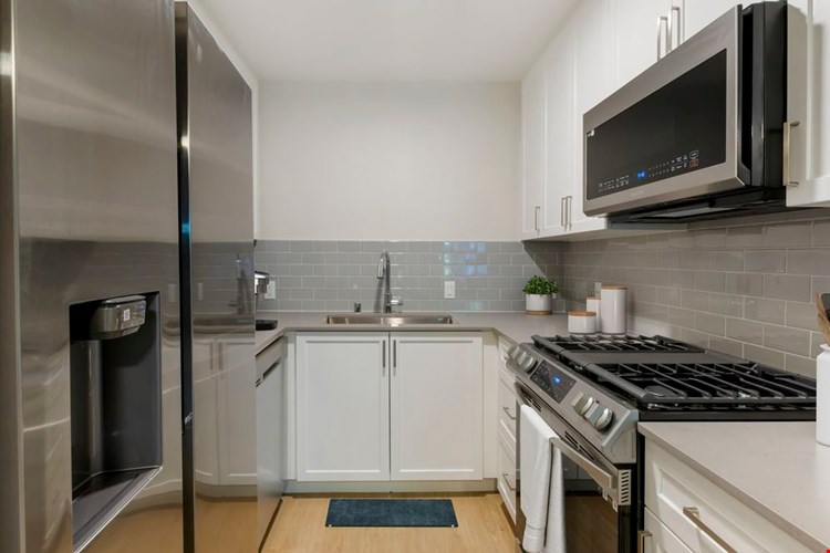 Kitchen with white cabinetry, grey quartz countertops, stainless steel appliances, grey tile backsplash, and hard surface flooring (Select Home)