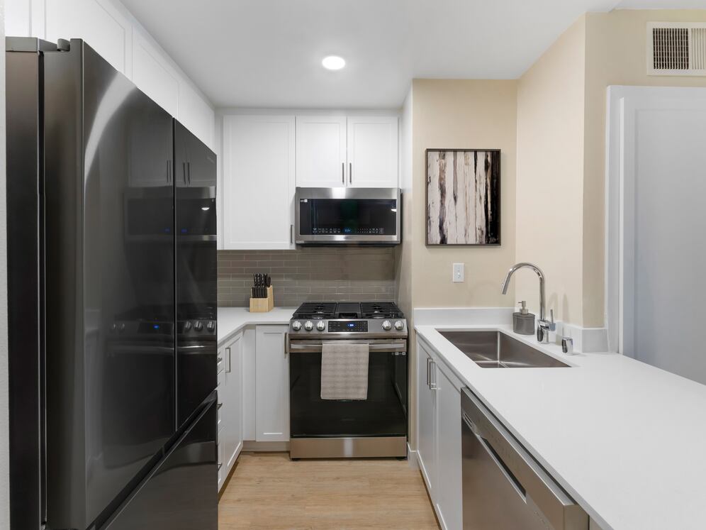 Renovated Package I kitchen with stainless steel appliances, white quartz countertops, white cabinetry, grey tile backsplash, and hard surface flooring