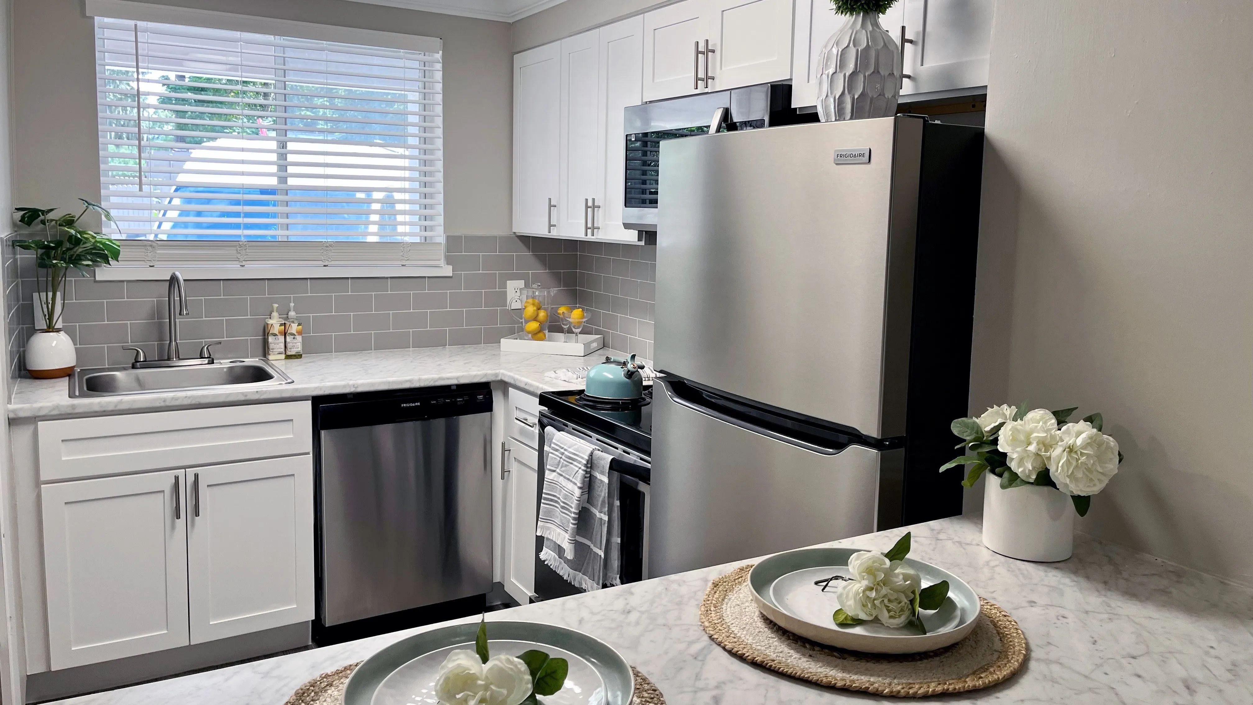 Indulge in the allure of elevated modern kitchen offerings adorned with luxurious white marble-inspired countertops, a sophisticated grey backsplash, and sleek white shaker cabinets. 