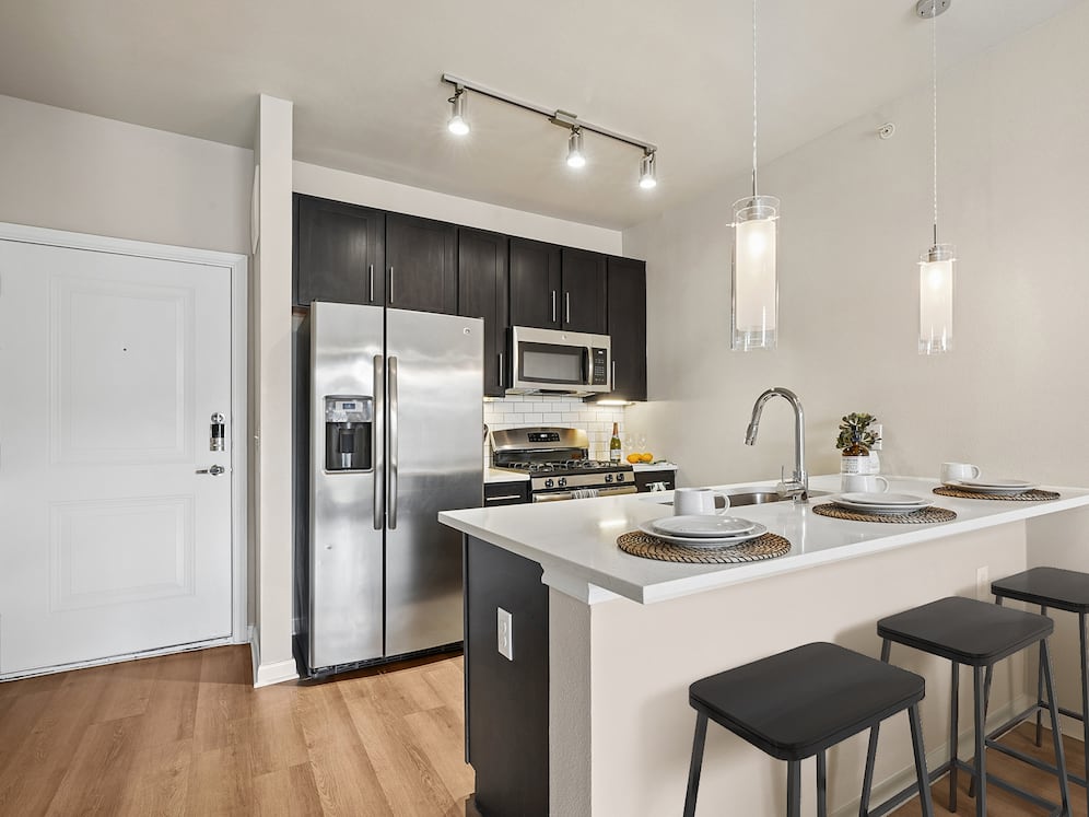 Kitchen with dark cabinetry, white quartz countertops, white subway tile backsplash, stainless steel appliances and hard surface flooring