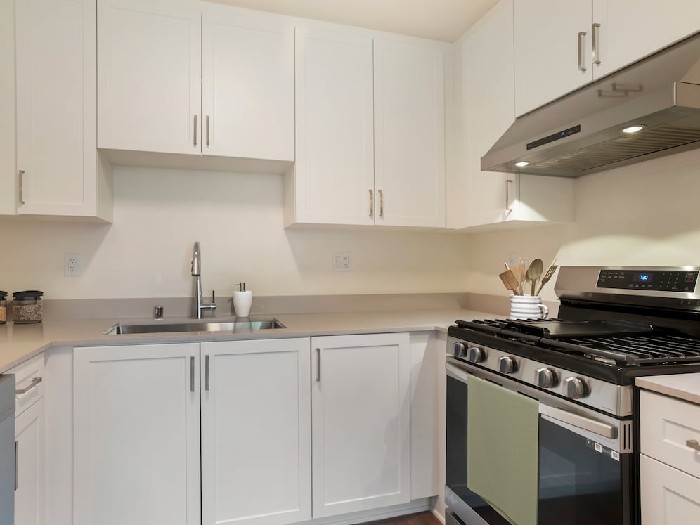Renovated Package I kitchen with stainless steel appliances, white cabinetry, beige granite countertops, and hard surface flooring