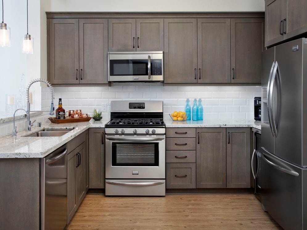 Kitchens with grey cabinetry, grey speckled granite countertops, white subway tile backsplash, stainless steel appliances, and hard surface flooring