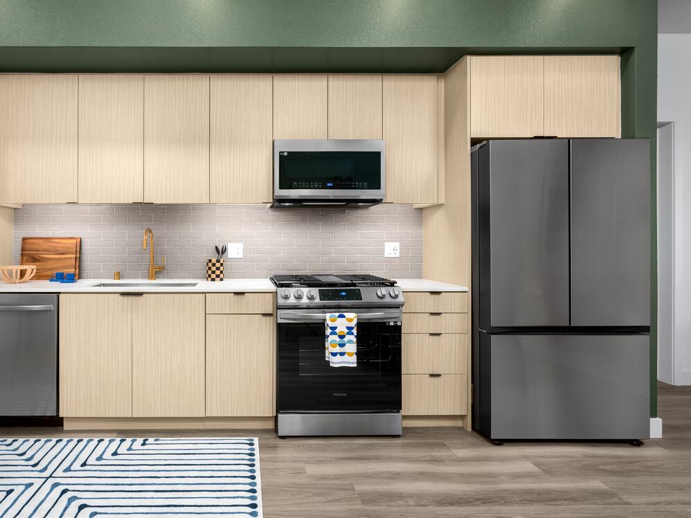 Finish Package I Kitchen with light oak cabinetry, white quartz countertop, grey tile backsplash, and stainless steel appliances