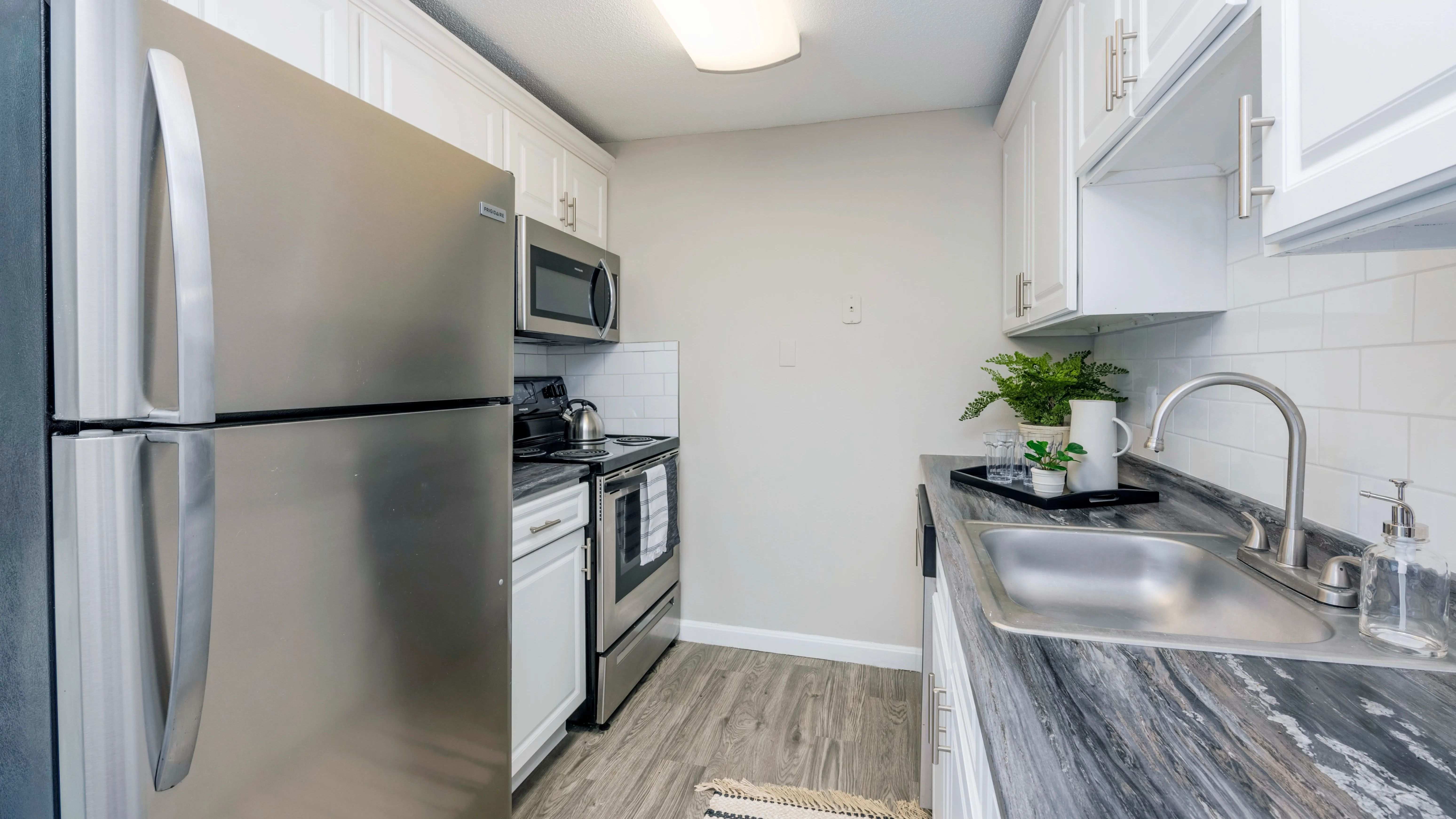 Indulge in modern elegance in The Sycamore Kitchen, boasting black fusion countertops, white cabinetry, and a stylish white subway tile backsplash.