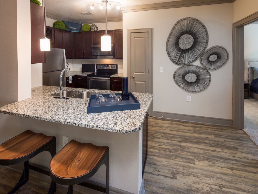 Modern kitchen with wood cabinetry, white tile backsplash, granite countertops, stainless steel appliances, and hard-surface flooring