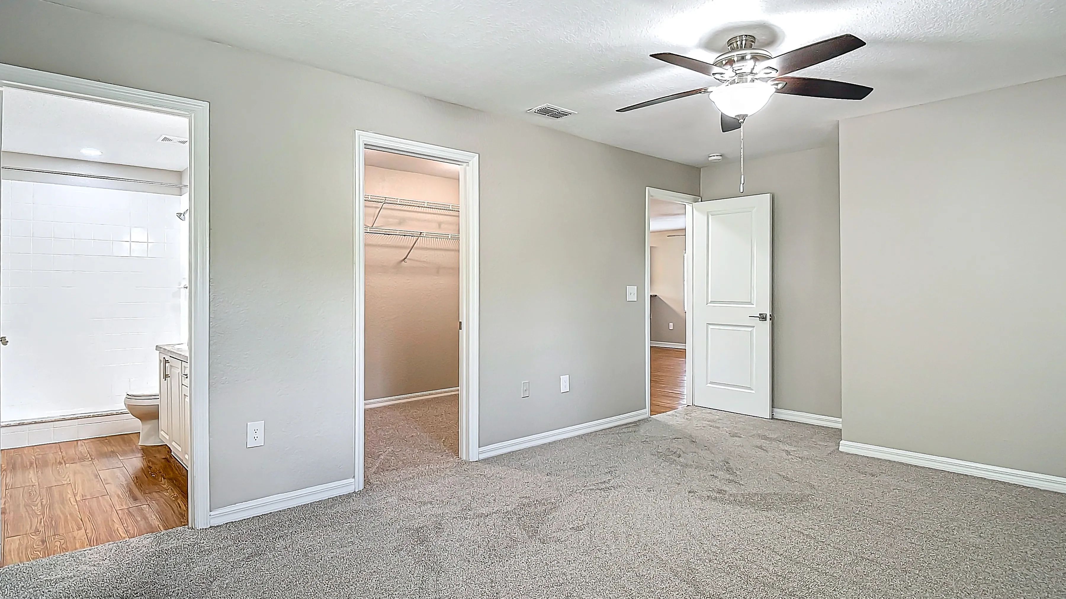 The master bedroom features a modern ceiling fan, plush carpeting, and easy access to both a large walk-in closet and a private en-suite bathroom.