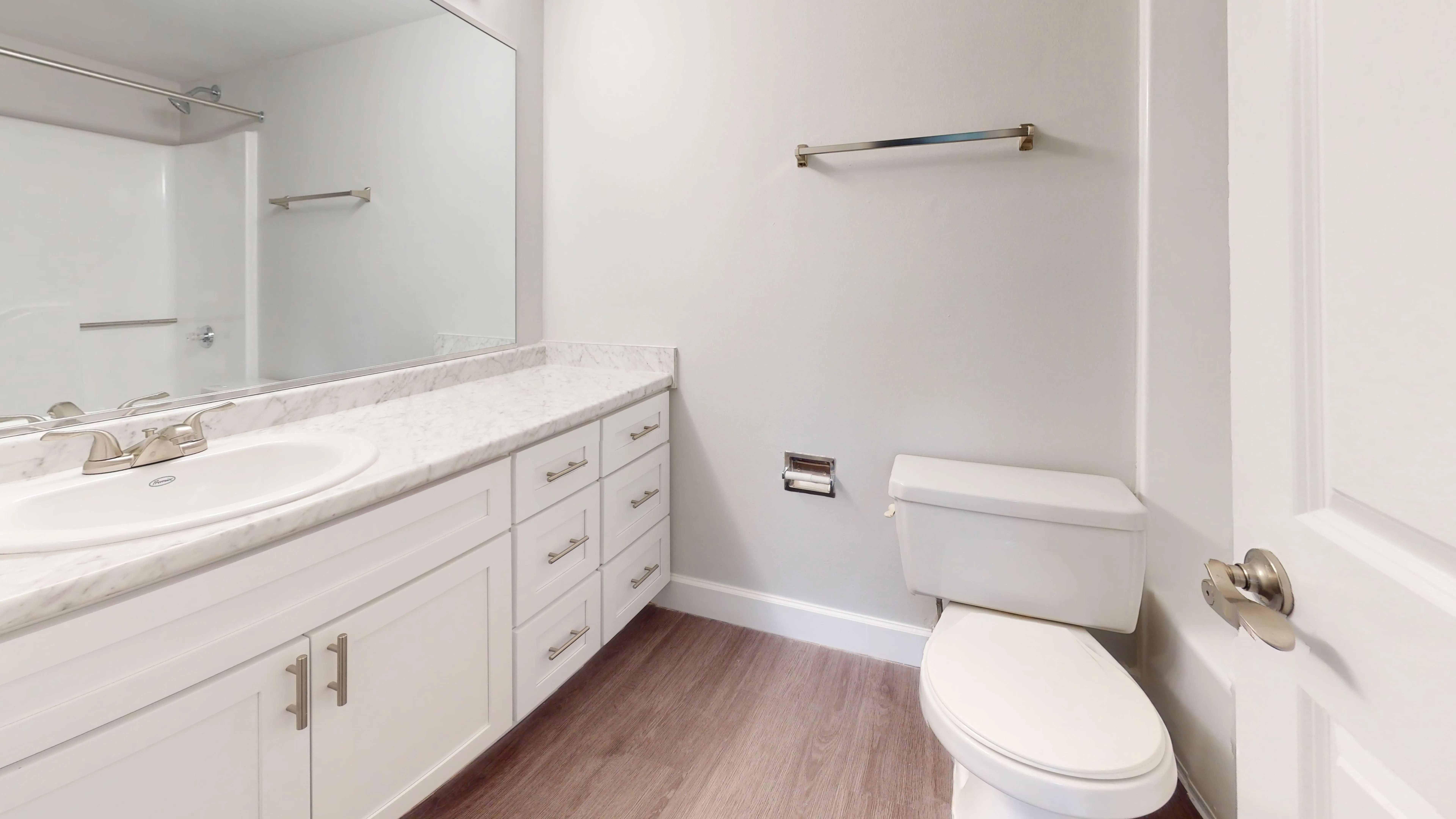 The Martinique floor plan at River Reach offers a modern bathroom with sleek white cabinetry, a large mirror, and beautiful marble-style countertops.