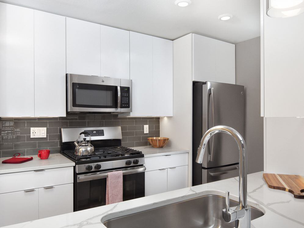 Premier Scheme kitchen with flat white cabinetry, white marbled quartz countertops, grey subway tile backsplash, stainless steel appliances, and hard surface flooring