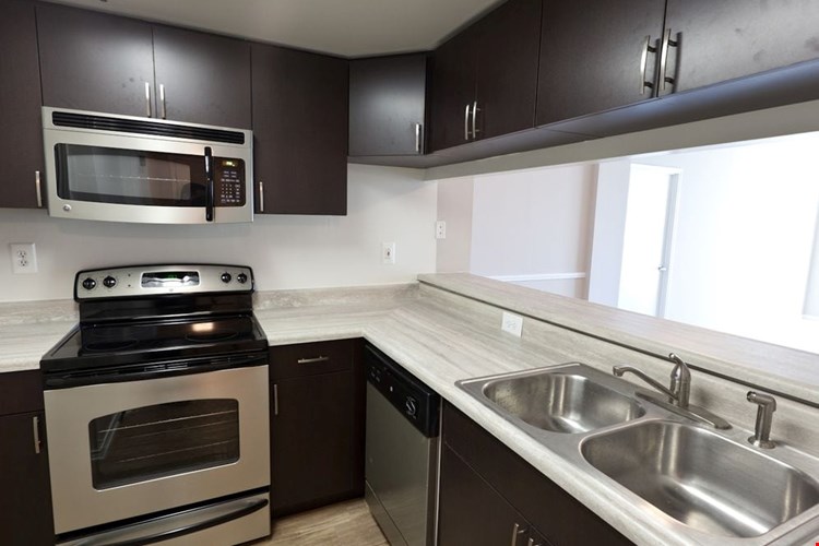 Classic Package II kitchen with grey countertops, espresso cabinetry, stainless-steel appliances, and hard surface flooring (select homes)