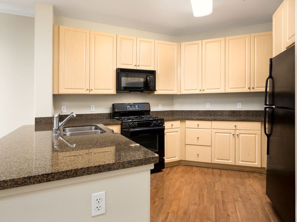 Classic Package I kitchen with oak cabinetry, granite countertops, black appliances, and hard surface flooring