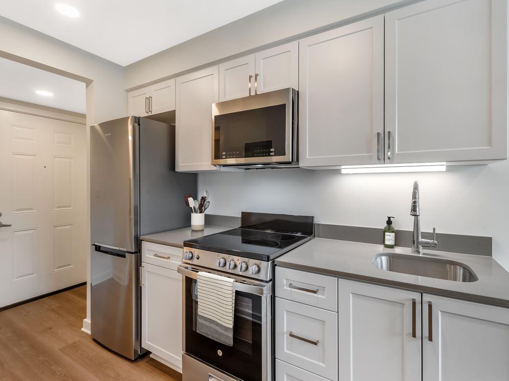 Renovated Package II kitchen with stainless steel appliances, light grey quartz countertops, white shaker cabinetry, and hard surface flooring